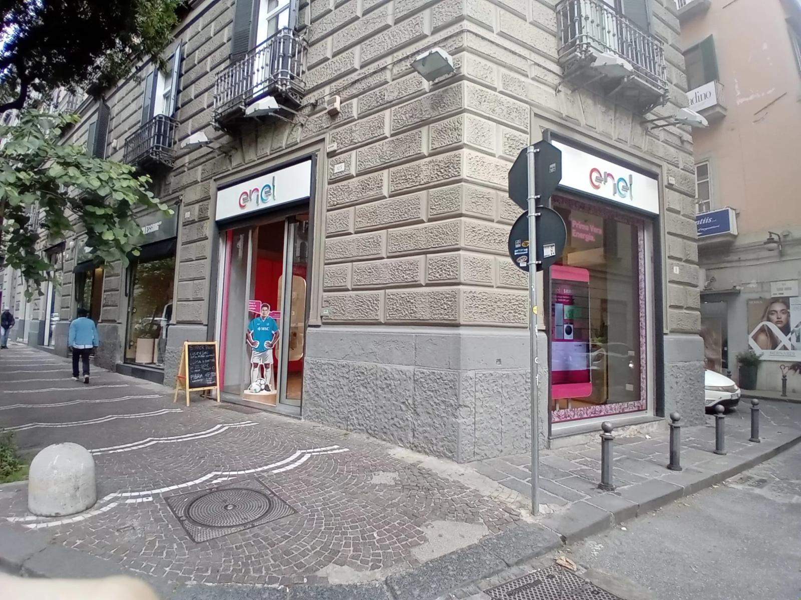 Facciata di giorno dello Spazio Enel Partner Napoli Corso Umberto I 123: vetrina fronte strada sul Rettifilo, insegna Enel visibile a luce naturale, edificio storico del centro di Napoli